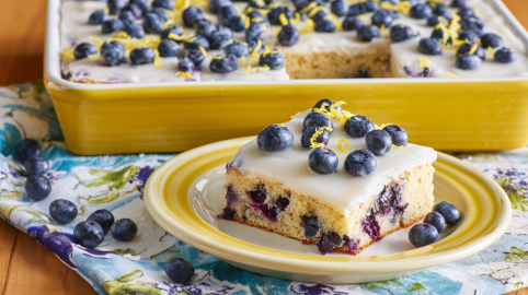 Ein Stück Blaubeer-Zitronen-Kuchen vom Blech. Im Hintergrund ist der restliche Kuchen.