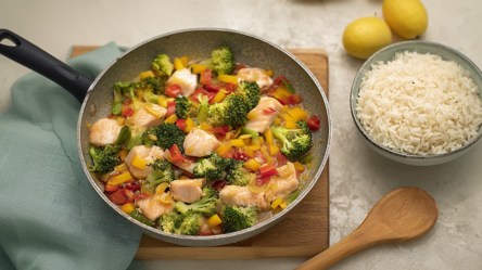 Eine Fischpfanne mit Gemüse, daneben eine Schüssel Reis.