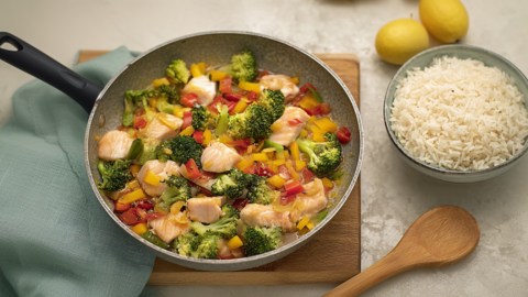 Eine Fischpfanne mit Gemüse, daneben eine Schüssel Reis.