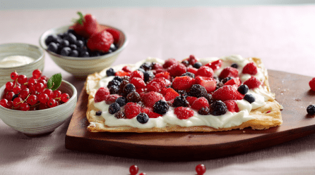 Flammkuchen mit Beeren, serviert auf einem Brett. Außen herum stehen Beeren auf einem Brett.