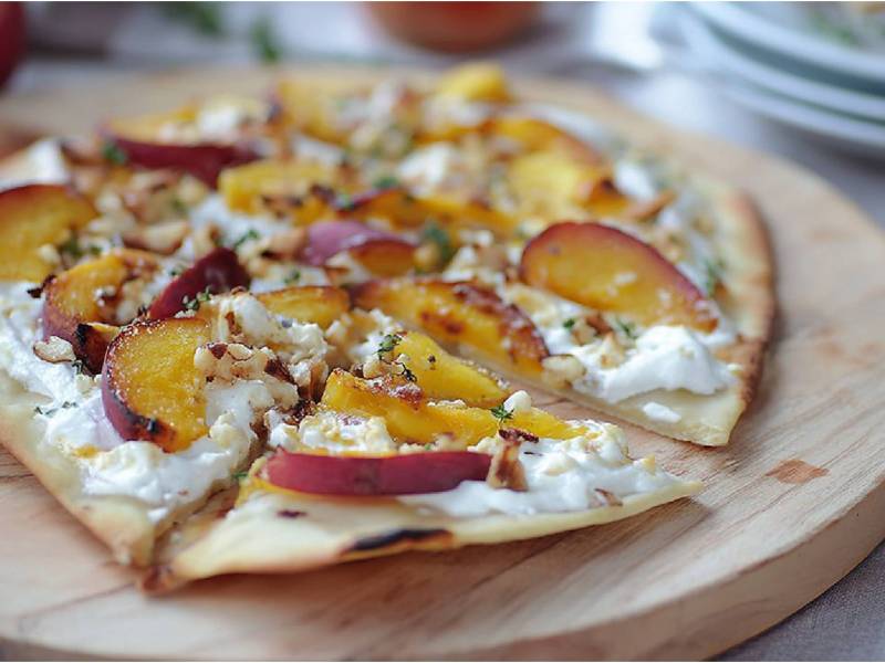 Brett mit einem in Stücke geschnittenen Flammkuchen mit Nektarinen und Ziegenkäse
