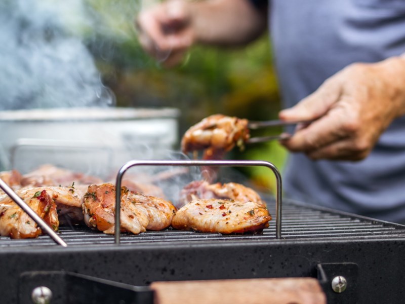 Mann wendet Fleisch, das an Grillrost klebt, mit einer Zange.