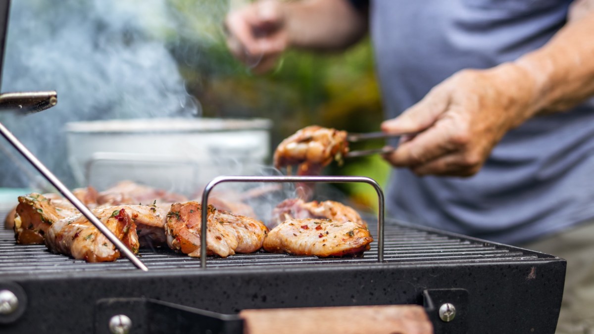 Mann wendet Fleisch, das an Grillrost klebt, mit einer Zange.