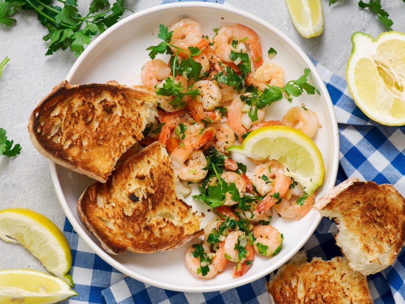 Ein Teller mit Garnelen mit Knoblauchbutter auf einer blau-weiß karierten Tischdecke.