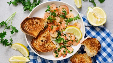 Ein Teller mit Garnelen mit Knoblauchbutter auf einer blau-weiß karierten Tischdecke.