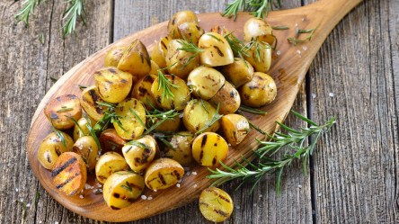 Eine große Portion gegrillte Kartoffeln mit Rosmarin auf einem Holzbrett.