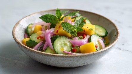 Ein Teller mit Gurken-Mango-Salat, der mit frischer Minze garniert ist.