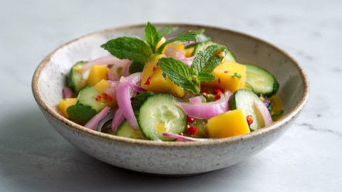 Ein Teller mit Gurken-Mango-Salat, der mit frischer Minze garniert ist.