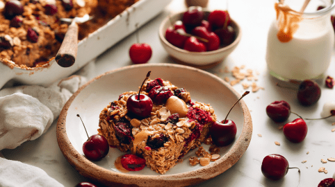 Ein Stück Haferflockenauflauf mit Kirschen auf einem Teller mit Rand.