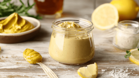 Ein Glas mit Honig-Senf-Aufstrich, drum herum liegen ein Löffel und eine Schale mit Senf, etwas Zitrone und Salz.