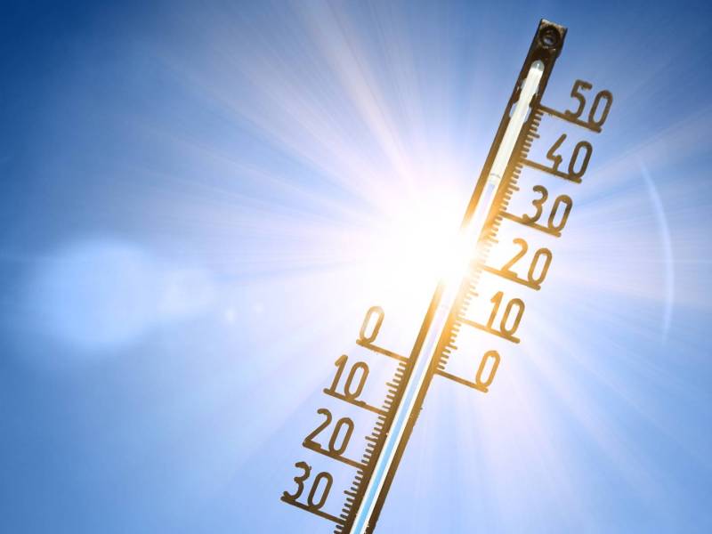 Ein Thermometer vor strahlend blauem Himmel und der Sonne. Das Bild steht metaphorisch für 