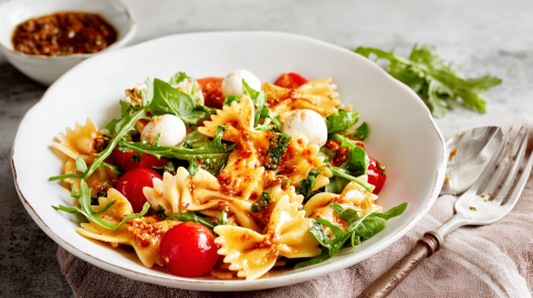 Ein tiefer Teller mit Nudelsalat mit Mozzarella und rotem Pesto.