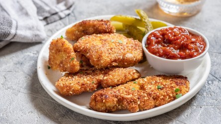 Ein Teller mit paniertem Kokos-Hähnchen, Gewürzgurken und einem Salsa-Dip.
