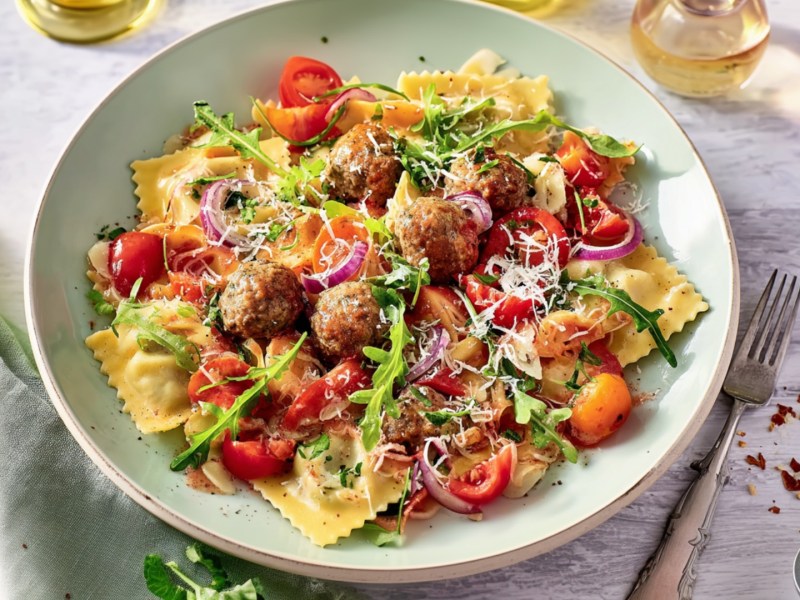 Ein Teller Ravioli vom Blech mit Gemüse, Hackbällchen und Rucola.