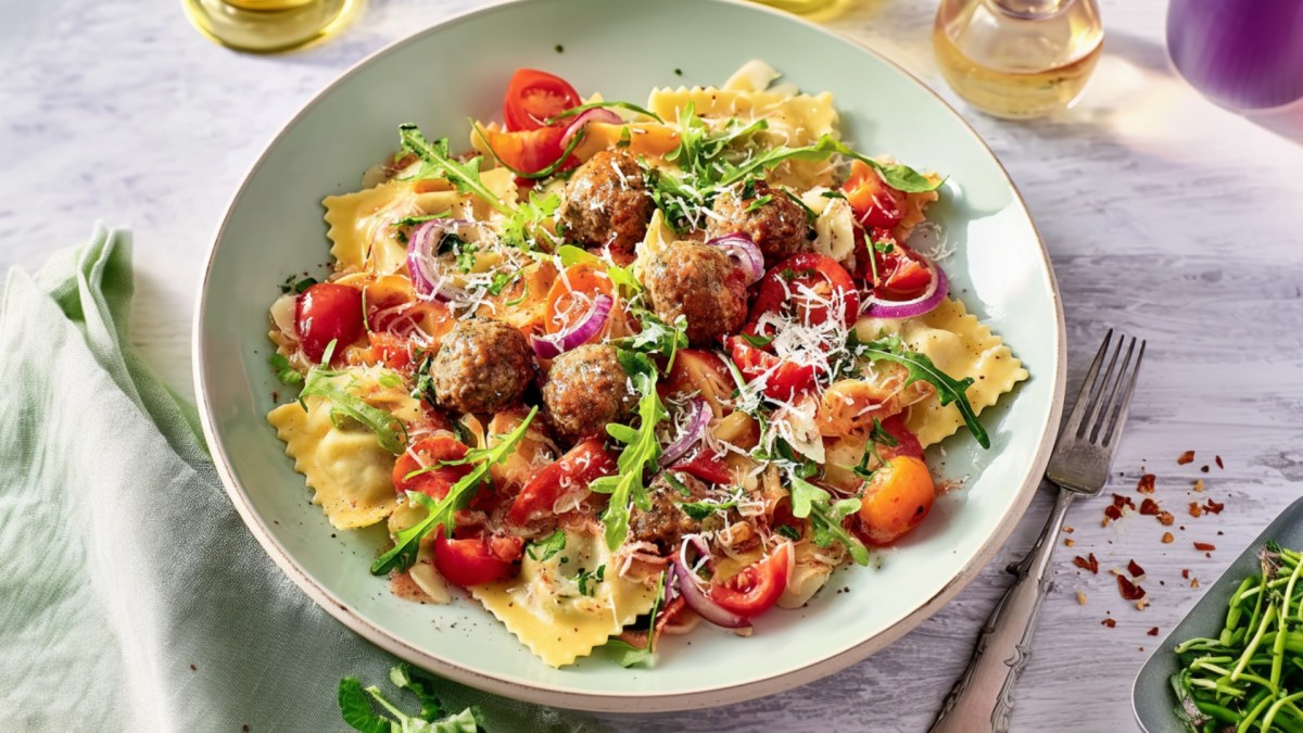 Ein Teller Ravioli vom Blech mit Gemüse, Hackbällchen und Rucola.