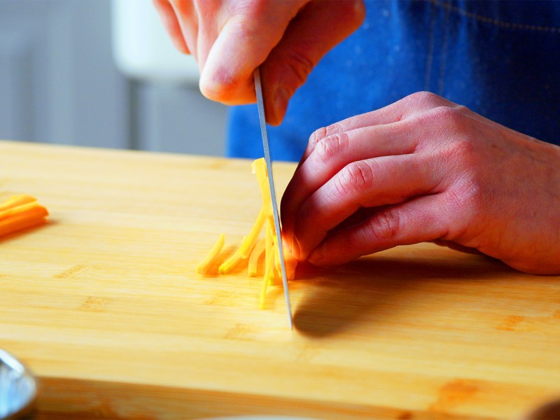 Schnittformen von Gemüse: Eine Köchin schneidet eine Möhre in dünne Streifen.