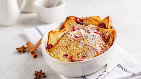 Toastbrotauflauf mit Himbeeren und Puderzucker in weißer Auflaufform, daneben Anissterne und Zimtstangen.