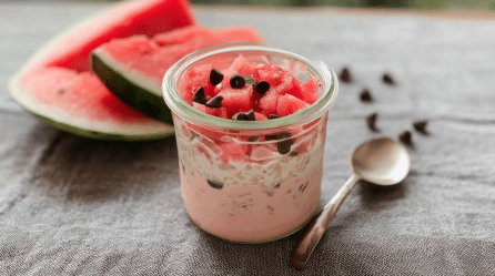 Ein Glas Wassermelonen-Overnight-Oats, daneben liegen Wassermelonenstücke nud Schokodrops.