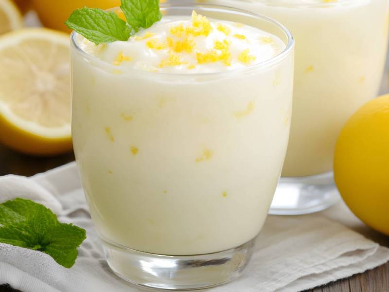 Zwei Gläser Zitronenquark auf einem Tisch, Zitronen daneben