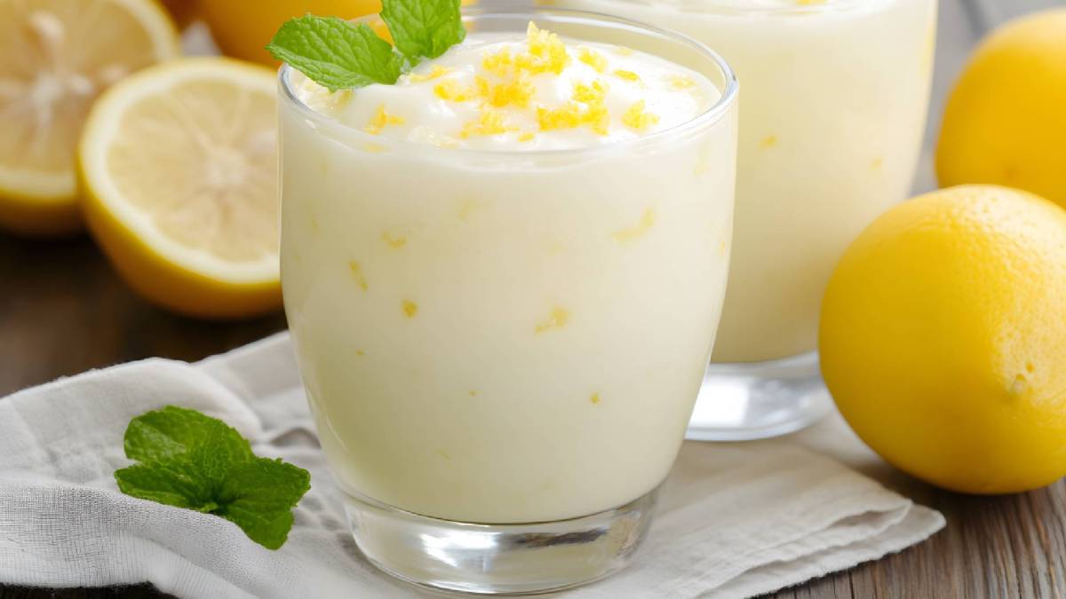 Zwei Gläser Zitronenquark auf einem Tisch, Zitronen daneben