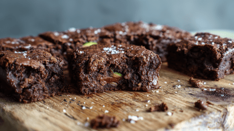 Mehrere Zucchini Brownies liegen auf einem Holzbrett. Sie sind angeschnitten und geben den Blick auf das Innere frei.