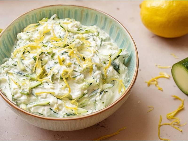 Schale mit Zucchini-Tzatziki, Zucchini und Zitrone daneben
