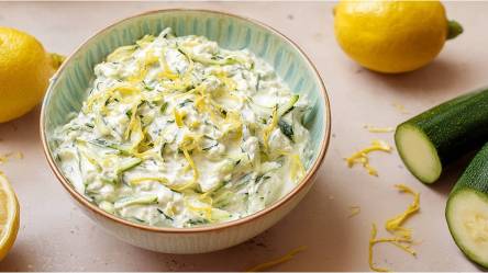 Schale mit Zucchini-Tzatziki, Zucchini und Zitrone daneben