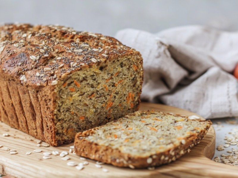 Ein angeschnittenes Apfel-Möhren-Brot auf einem Holzbrett.