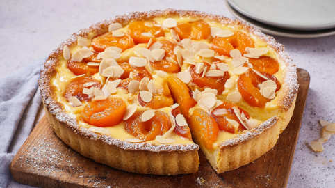 Aprikosen-Schmand-Tarte mit Mandelblättchen auf einem Holzbrett.