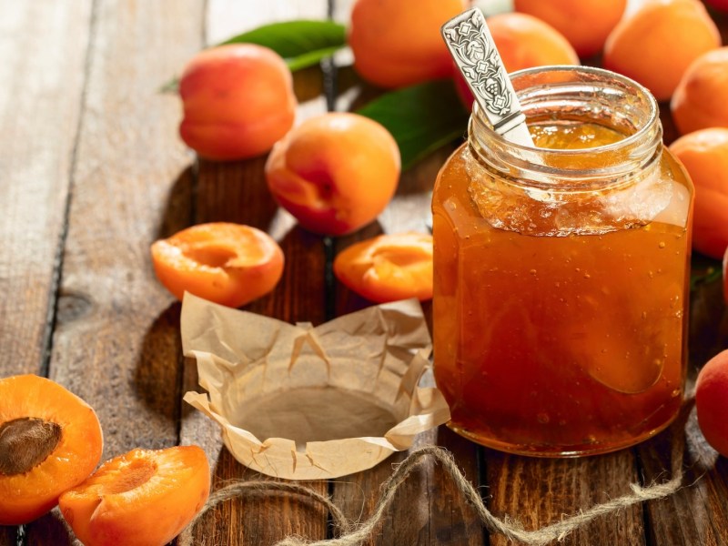 Ein Glas Aprikosenmarmelade, umgeben von einigen Aprikosen.