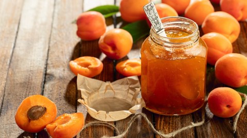 Ein Glas Aprikosenmarmelade, umgeben von einigen Aprikosen.