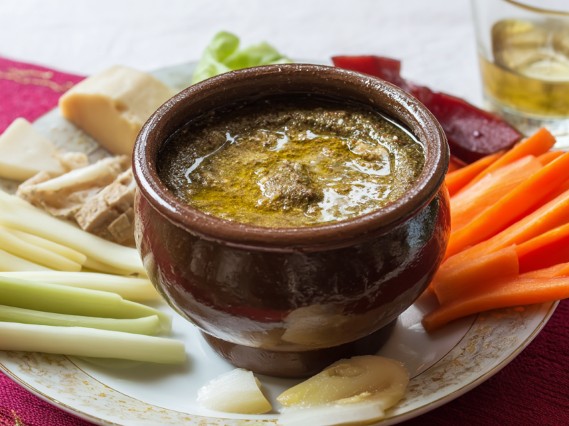 Eine TOnschale mit Bagna Cauda: italienischem Sardellen-Dip. Drum herum sind Gemüsesticks und Käsestückchen angeordnet.