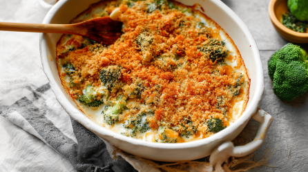 Eine ovale Auflaufform mit Brokkoli-Käse-Auflauf und einem Holzlöffel darin.