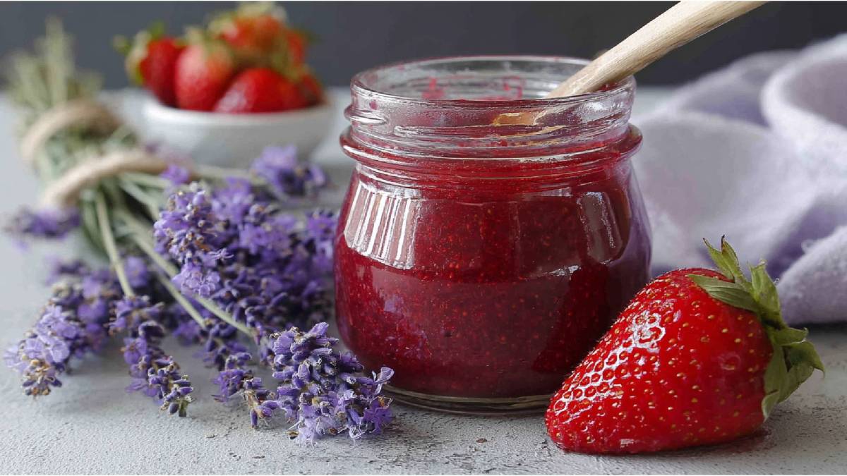 Glas mit Erdbeer-Lavendel-Marmelade auf einem Tisch, Strauß Lavendel und frische Erdbeeren daneben