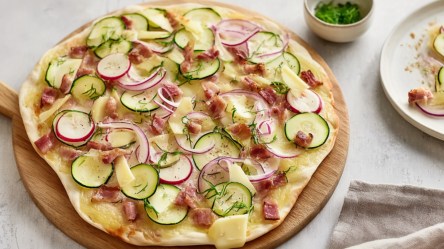 Ein Flammkuchen mit Zucchini vom Grill auf einem Holzbrett.