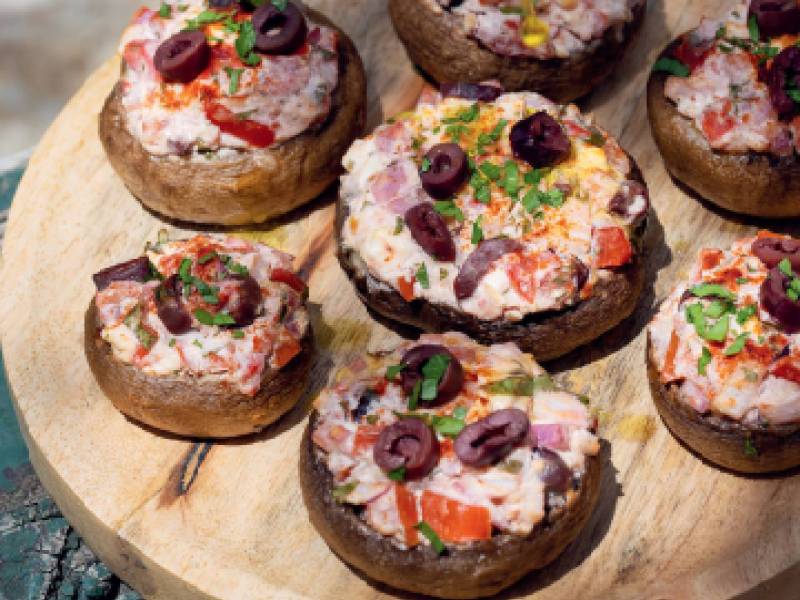 Küchenbrett mit gefüllten Pilzen mit Fetakäse und Tomaten