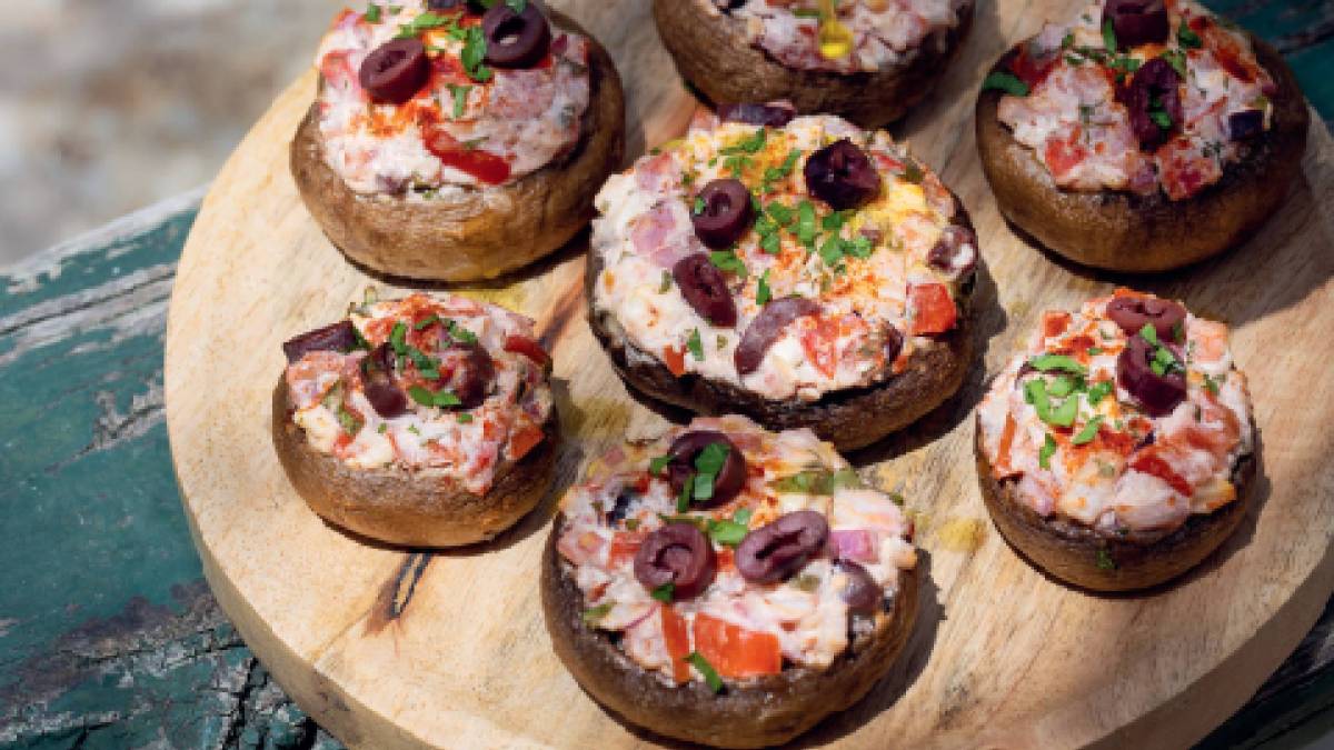 Küchenbrett mit gefüllten Pilzen mit Fetakäse und Tomaten