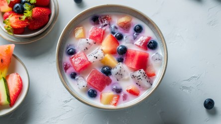 Eine Schüssel koreanische Wassermelonen-Kaltschale, Hwachae. Links im Bild sind Schalen mit frischen Früchten wie Beeren und Wassermelone zu sehen.