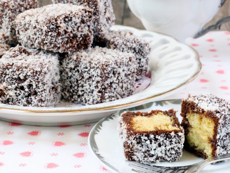 Ein Teller mit Lamingtons: australischen Kuchenwürfeln. Davor liegt ein aufgeschnittener Würfel.