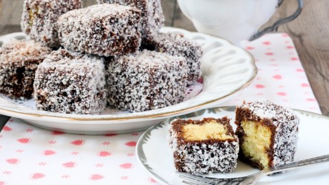 Ein Teller mit Lamingtons: australischen Kuchenwürfeln. Davor liegt ein aufgeschnittener Würfel.