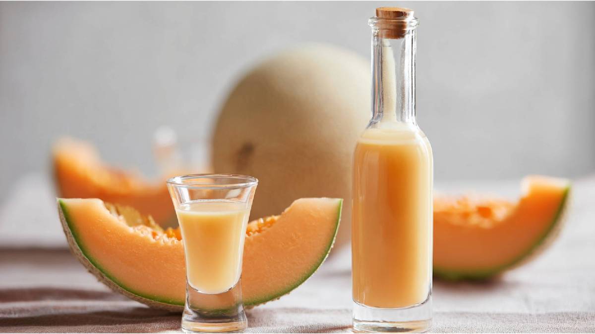 Eine Flasche und ein Glas mit Meloncello, dahinter eine aufgeschnittene Melone