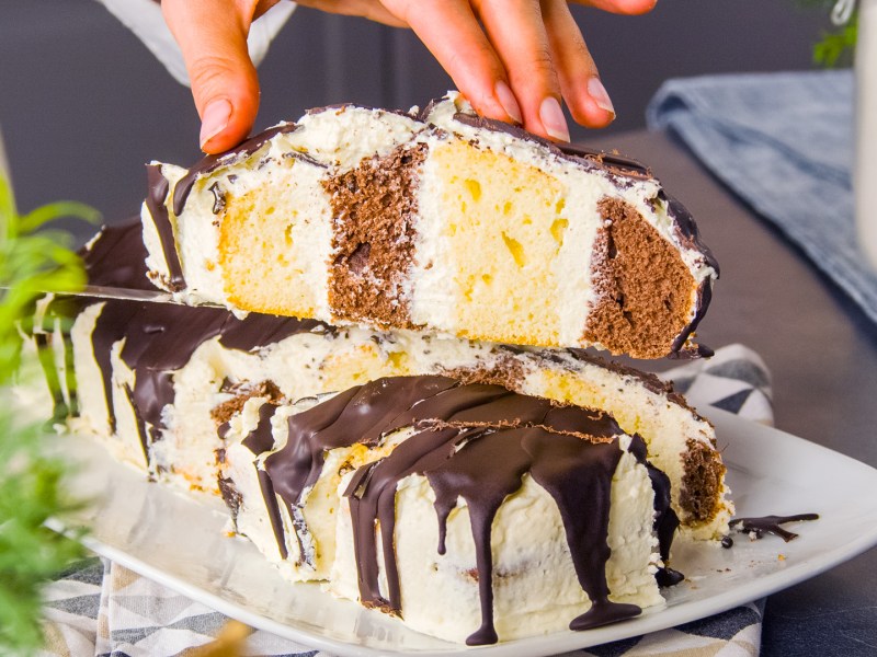Ein Stück Metrowiec wird in die Kamera gehalten. Dahinter ist der restliche Kuchen zu sehen.