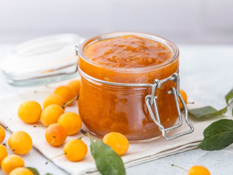 Ein Glas Mirabellenmarmelade. Daneben liegen frische Früchte.