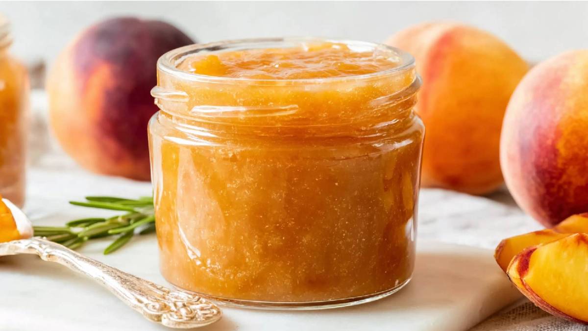 Glas Pfirsich-Rosmarin-Marmelade mit frischen Pfirsichen im Hintergrund