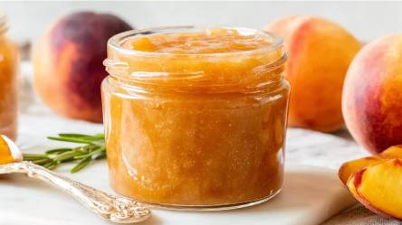 Glas Pfirsich-Rosmarin-Marmelade mit frischen Pfirsichen im Hintergrund