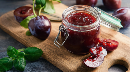 Ein Glas Pflaumen-Basilikum-Marmelade auf einem Holzbrett.