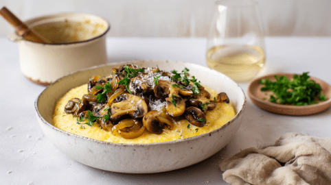 Ein Teller mit Pilzragout mit Parmesan-Polenta. Daneben liegt eine Serviette und steht ein Glas Wein.