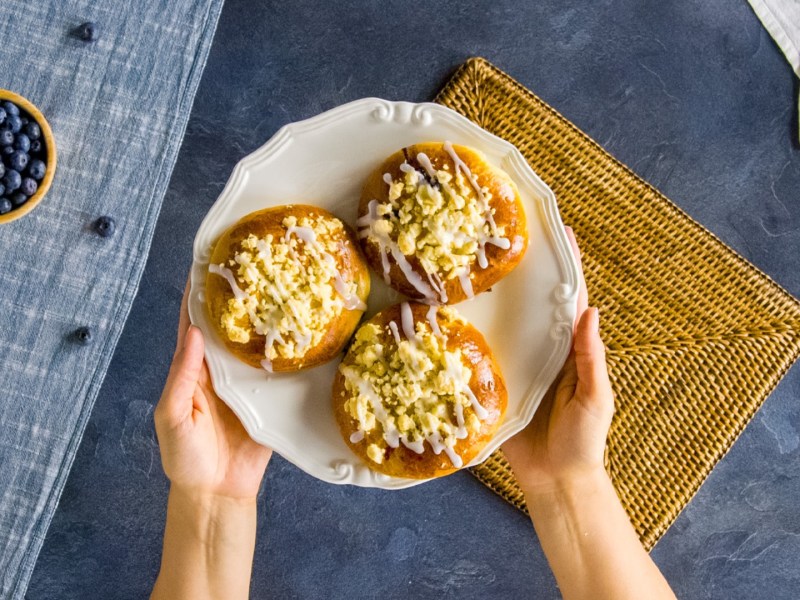 Drei polnische Blaubeerbrötchen auf einem Teller, der von zwei Händen gehalten wird.