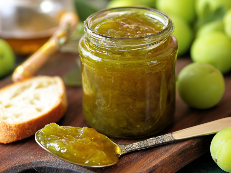 Ein Glas Renekloden-Marmelade, daneben eine Scheibe Brot und einige Renekloden.