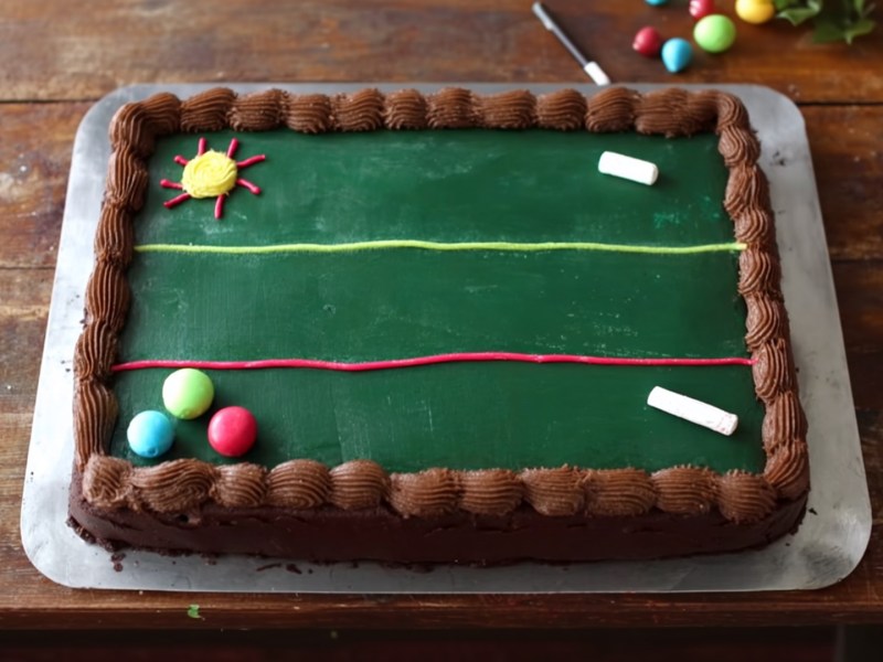 Ein Schultafel-Kuchen, der auf einer silbernen Servierplatte liegt. Der Kuchen ist mit Lebensmittel und Fondant verziert.